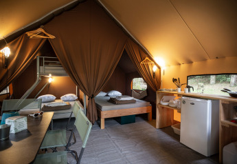 Vista interna di una tenda safari con letti, angolo cucina e tavolo da pranzo in ambiente naturale.