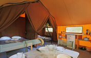 Vista interior de una tienda safari con camas, mesa de comedor y cocina para una experiencia cómoda.
