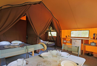Intérieur d'une tente safari avec lits, table à manger et kitchenette pour un séjour de camping confortable.
