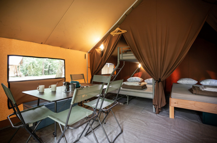 Interior de tienda safari con mesa de comedor, sillas, utensilios de cocina y cómodas camas para descansar.