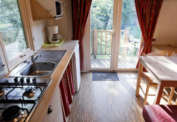 Acogedora cocina de cabaña con fogón, cafetera, mesa de comedor y puertas de cristal hacia un jardín verde.