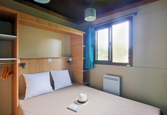 Schlafzimmer im Chalet Evasion bei Huttopia Landes Sud, Frankreich, mit Doppelbett und großem Fenster.