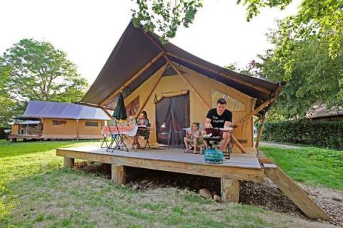 Famiglia che si rilassa sulla veranda di una tenda safari Trappeur II, circondata dal verde.