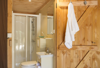 Badkamer in een Trappeur II safaritent bij Huttopia Etang de Fouché, Frankrijk, met houten deur en douche.