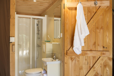 Baño en una tienda Trappeur II en Huttopia Etang de Fouché, Francia, con puerta de madera y ducha.