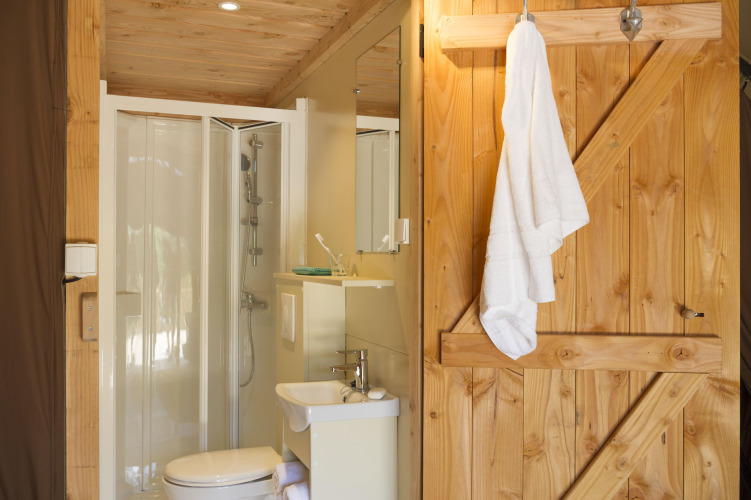 Baño en una tienda Trappeur II en Huttopia Etang de Fouché, Francia, con puerta de madera y ducha.