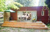 Eine moderne Holzhütte mit großer Terrasse, Gartenmöbeln, Grill und Sonnenschirm im Grünen.