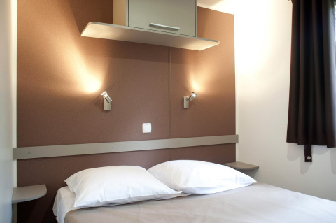 Modernes Schlafzimmer in einer Hütte mit Doppelbett, weißen Kissen, Wandlampen und braunen Wänden.