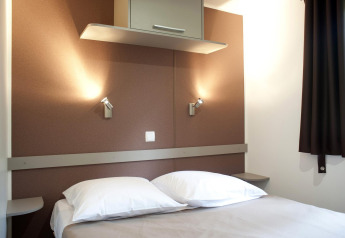 Dormitorio moderno de cabaña con cama doble, almohadas blancas, lámparas de pared y paredes marrones.