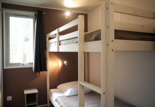 Een eenvoudige kajuitkamer met houten stapelbedden, een raam met gordijn en een klein nachtkastje.