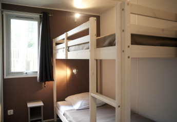 Habitación de cabaña sencilla con literas de madera, ventana con cortina y una pequeña mesa de noche.