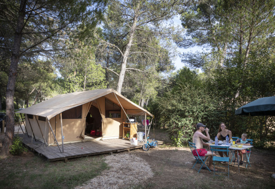 Family enjoying breakfast at a table in front of a safari bungalow tent at Huttopia Fontvieille, France.