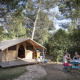 Familie, der nyder morgenmad ved et bord foran en safaritelthytte i skovene ved Huttopia Fontvieille, Frankrig.