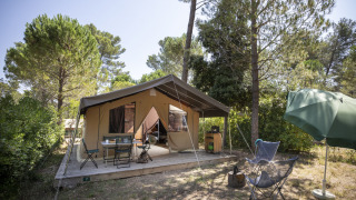 Tenda safari Toile&Bois Sweet al campeggio nella foresta, con veranda, sedie da esterno e ombrellone verde.