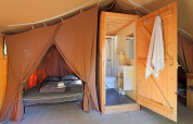 Innenansicht eines Safari-Tents vom Typ Toile&Bois mit Doppelbett und privatem Badezimmer mit Dusche.