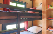 Glampingværelse med køjesenge, træreoler, opbevaringshylder og vinduer med røde gardiner i dagslys.
