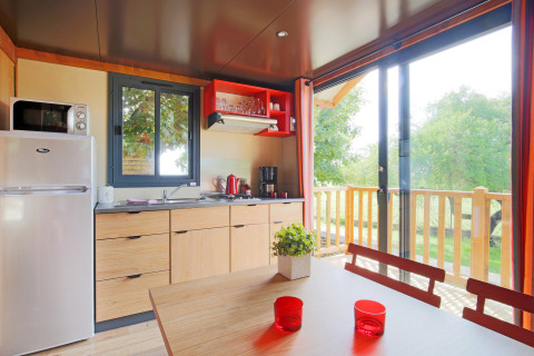 Cocina y comedor luminosos en una cabaña con vistas a una terraza verde en Roulotte, Huttopia Fontvieille, Francia.