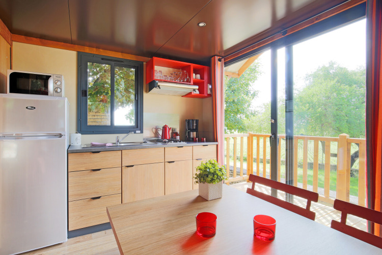 Cuisine lumineuse et salle à manger dans une cabane avec vue sur la terrasse de Roulotte, Huttopia Fontvieille, France.