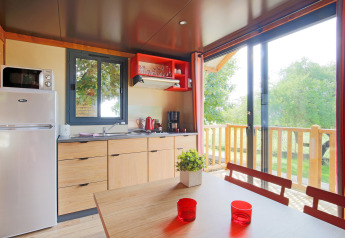 Cocina y comedor luminosos en una cabaña con vistas a una terraza verde en Roulotte, Huttopia Fontvieille, Francia.