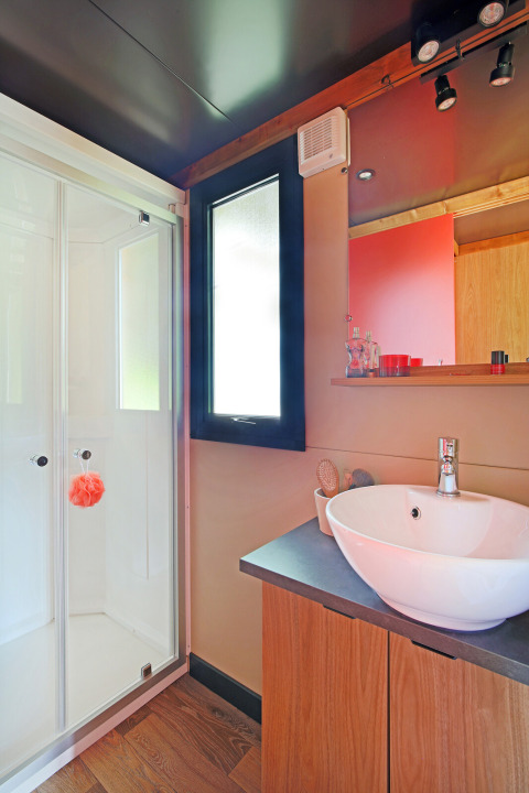 Modernes Badezimmer in einer Hütte, mit Duschkabine, Waschbecken, Holzunterschrank und Spiegel.