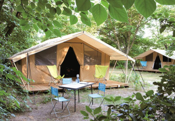 Tienda safari Toile&bois Classic en la naturaleza, con terraza de madera, sillas y mesa de camping.