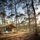 Safari-telt Toile&Bois Tent Sweet i en skov med sollys, veranda og campingstole foran teltet.