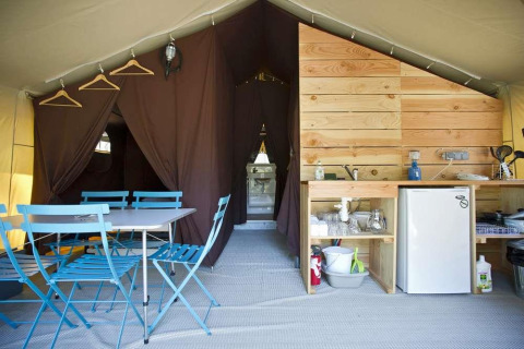 Interior de una tienda Toile&Bois con comedor y cocina en Huttopia Lac de Carcans en Francia.