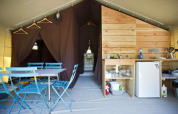 Interior de una tienda Toile&Bois con comedor y cocina en Huttopia Lac de Carcans en Francia.