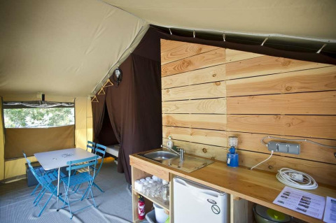 Foto interior de la tienda safari Toile&Bois Sweet en Huttopia Lac de Carcans con comedor y zona de cocina.