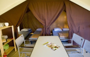 Interior of a safari tent featuring four single beds, a dining table, chairs, and shelves for glamping.