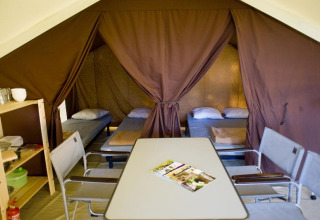 Interior de una tienda safari con cuatro camas individuales, mesa de comedor, sillas y estantería organizada.