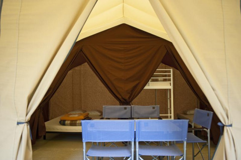 Foto interior de una tienda safari con camas y sillas, Toile&bois tent Classic en Huttopia Oléron les Pins, Francia.