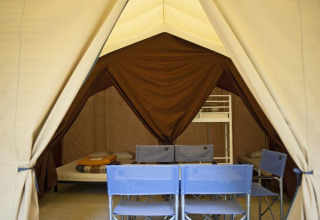 Foto interior de una tienda safari con camas y sillas, Toile&bois tent Classic en Huttopia Oléron les Pins, Francia.