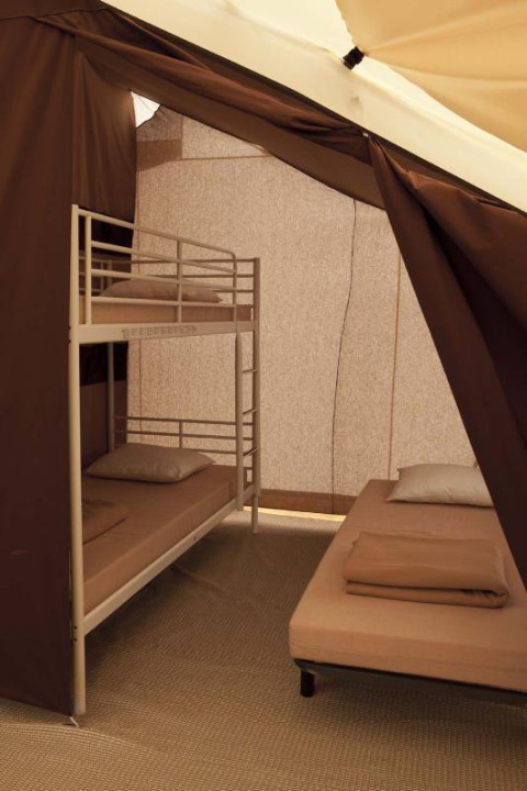 Interior view of a safari tent with a bunk bed and a single bed at Huttopia Oléron les Pins, France.