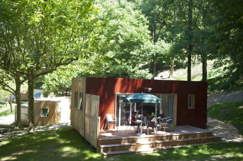 Mobil-home Vancouver à Huttopia Sarlat en France, entouré d'arbres et de nature, des personnes sur la terrasse.