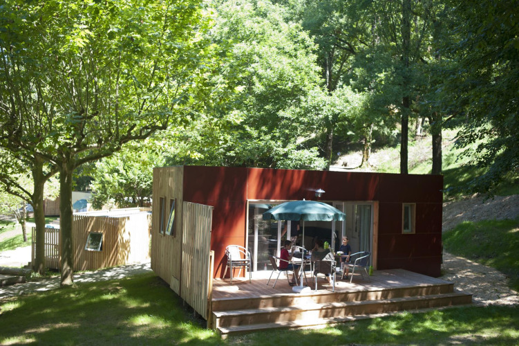 Mobile home Vancouver at Huttopia Sarlat, France, surrounded by lush trees and nature, with people relaxing.