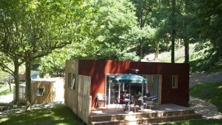 Mobil-home Vancouver à Huttopia Sarlat en France, entouré d'arbres et de nature, des personnes sur la terrasse.