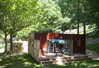 Mobil-home Vancouver à Huttopia Sarlat en France, entouré d'arbres et de nature, des personnes sur la terrasse.
