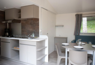 Cuisine moderne de cabane et coin repas, table dressée pour quatre, tons neutres et grande fenêtre.