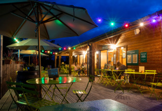 Udendørs caféområde ved Huttopia Etang de Fouché i Bourgogne, Frankrig med farverige lyskæder om aftenen.