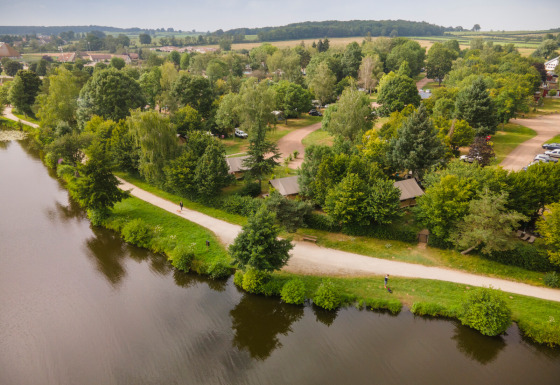 Luftfoto af Huttopia Etang de Fouché feriepark i Bourgogne-Franche-Comté, Frankrig ved en rolig sø.