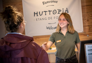 Receptionist byder gæst velkommen ved skranken på Huttopia Etang de Fouché i Bourgogne, Frankrig.