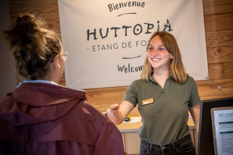 Receptionist welcomes guest at the desk in Huttopia Etang de Fouché holiday park, Bourgogne, France.