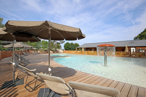 Outdoor pool area with sun loungers and umbrellas at Huttopia Etang de Fouché holiday park in Burgundy, France.