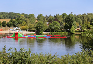 Parque acuático inflable en un lago rodeado de árboles en Huttopia Etang de Fouché, parque de vacaciones en Francia.