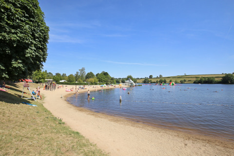 Strand aan een meer met bezoekers in het vakantiepark Huttopia Etang de Fouché, Bourgogne, Frankrijk.