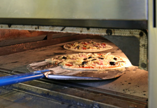 Pizza che cuoce in un forno a pietra a Huttopia Etang de Fouché, parco vacanze in Borgogna-Franca Contea, Francia.