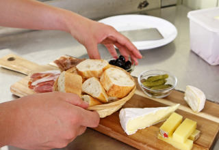 Une personne prépare un plateau avec du pain, des fromages, de la charcuterie, des olives et cornichons.