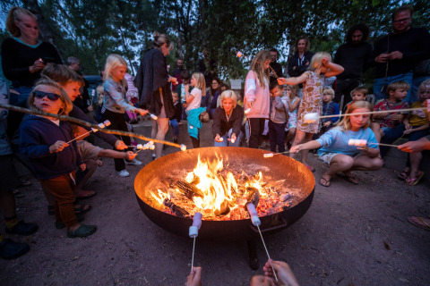 Børn og voksne rister skumfiduser over et bål i ferieparken Huttopia Etang de Fouché i Frankrig.