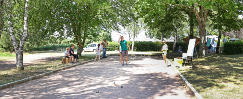 Visitantes juegan petanca bajo los árboles en el parque vacacional Huttopia Etang de Fouché, Borgoña, Francia.